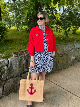 Woman in a navy and white printed  dress with red jean jacket standing on a sidewalk