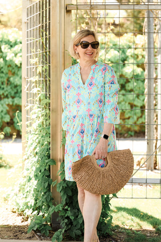 Woman in a colorful dress holding a straw bag outdoors.
