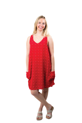 A woman wearing a red sleeveless mini dress with a V-neckline and side pockets, featuring Swiss-dot pom detail.