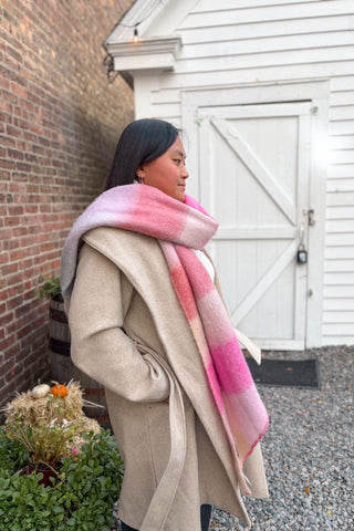 Woman wearing a pink and beige plaid scarf in front of a white building.
