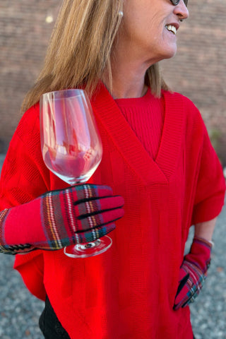 Person wearing a red sweater and plaid gloves holding a wine glass.