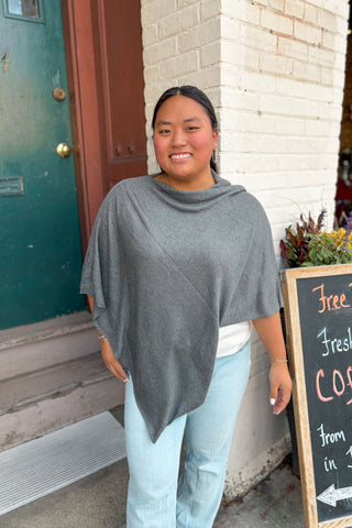 Woman wearing a gray poncho standing outside a building with a chalkboard sign.