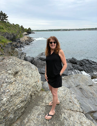 Woman in a black eyelet V-neck top and matching skort standing on rocky coastal area