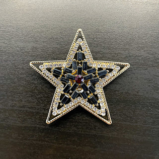 Gold star-shaped brooch with clear, navy and red gemstones