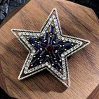 Silver star-shaped magnetic brooch  decorated with black gemstone and clear rhinestones.