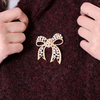 Gold bow-shaped magnetic brooch decorated with pearls and rhinestones.
