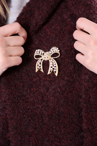 Magnetic gold bow brooch with pearl accents on burgundy scarf