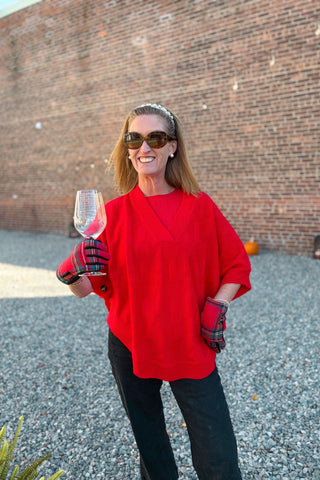 Woman in a red sweater holding a wine glass against a brick wall.