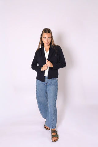 Person wearing a black cardigan and blue jeans on a white background
