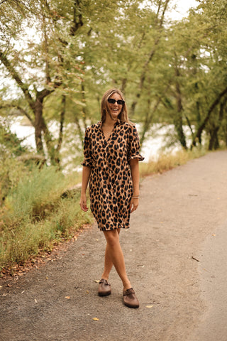 Woman in a leopard print dress standing on a path surrounded by trees