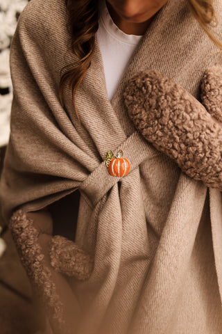 Close-up of a person wearing a brown coat with a decorative brooch on a blurred background