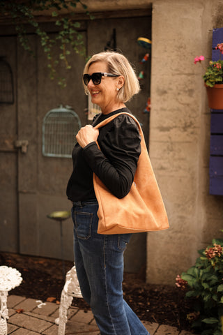 Woman holding a peach tote bag outdoors with a neutral background