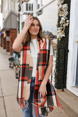 Woman wearing a plaid scarf on a street with buildings and decorative elements in the background