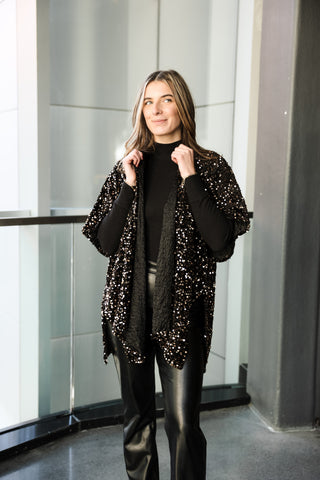 Woman wearing a black sequin cardigan over a black top and leather pants in an indoor setting.