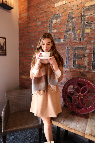 Woman holding a cup in front of a brick wall with 'Cafe' sign
