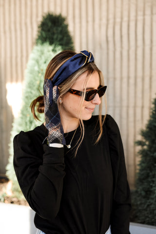 Woman wearing a blue headband with plaid pattern, sunglasses, and black top in front of a Christmas tree.