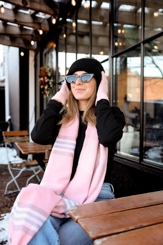 Woman wearing a pink scarf, black beanie, and sunglasses in an outdoor setting.