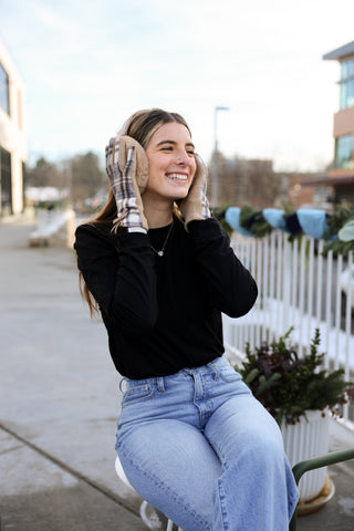 Woman sitting outdoors wearing a black sweater and blue jeans, with a blurred background.
