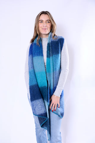 Woman wearing the Anne Scarf in bold wide blue stripes, styled over a light gray top and jeans.