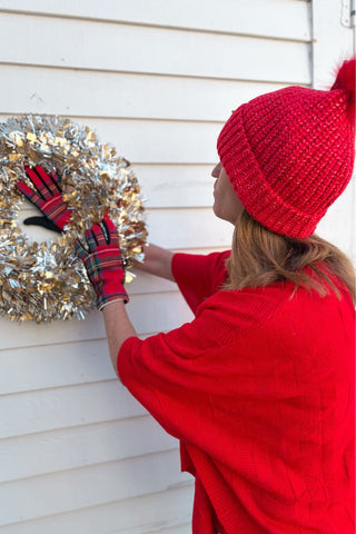 Person in red outfit and gloves hanging a decorative wreath on a door.