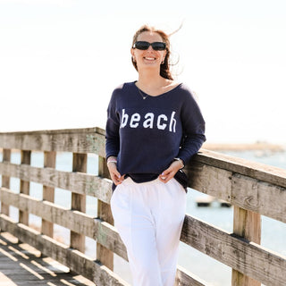 Woman wearing navy sweater with the word beach written across the front