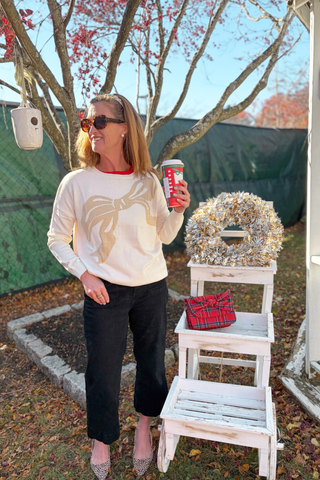 Cream Sweater Image: Woman wearing cream Madeline Holiday Bow Sweater with gold bow detail – cozy and stylish holiday outfit.